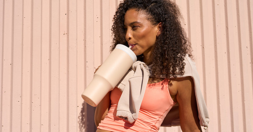 Sporty woman wearing stylish, athletic clothing drinking from an Owala 40oz Tumbler set in a sunny, outdoors scene - showcasing drinkware perfect for convenient, everyday hydration.