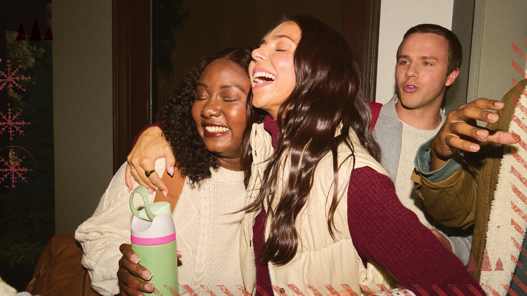 Two women laughing and hugging at a holiday gathering, one holding a mint green Owala bottle