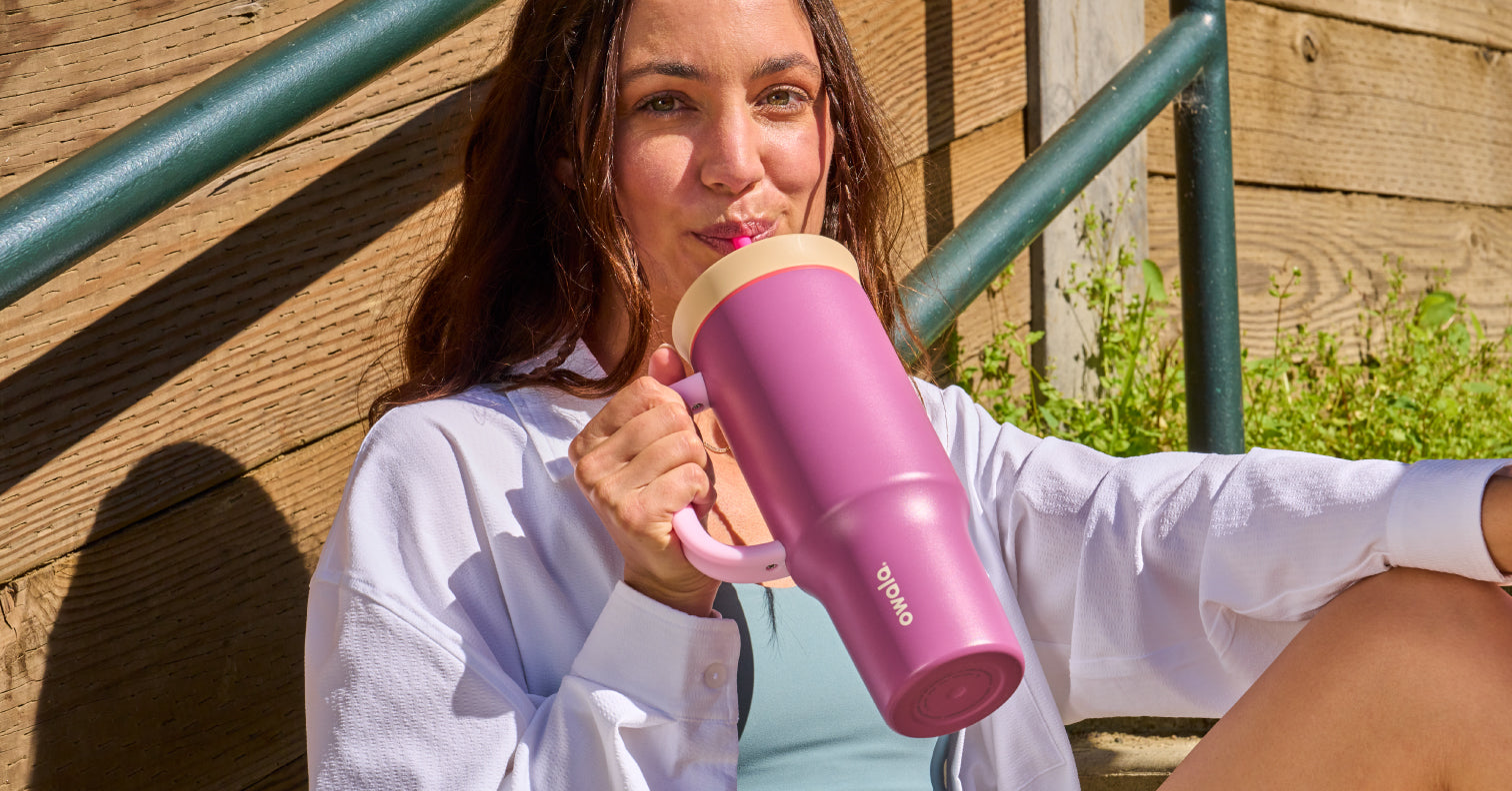 Stylish young woman sipping from a colorful magenta 40oz Owala tumbler, featuring a sunny, urban background -- exciting drinkware for effortless hydration