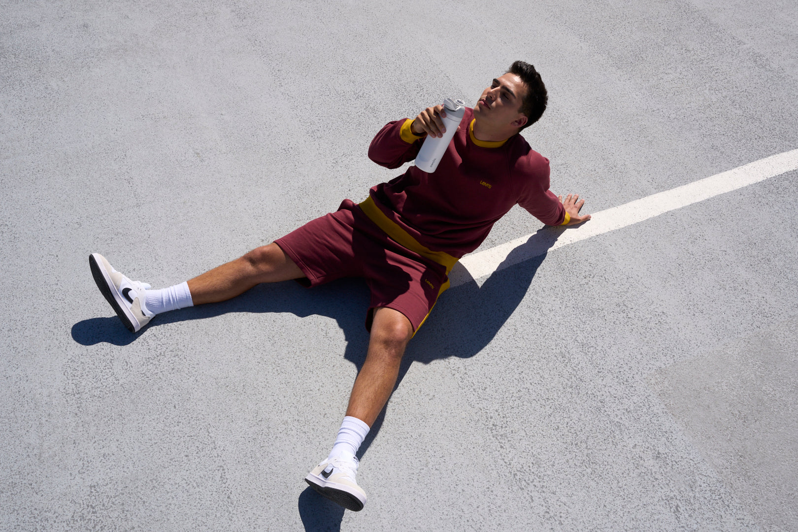 Man drinking water sitting on a sports court.