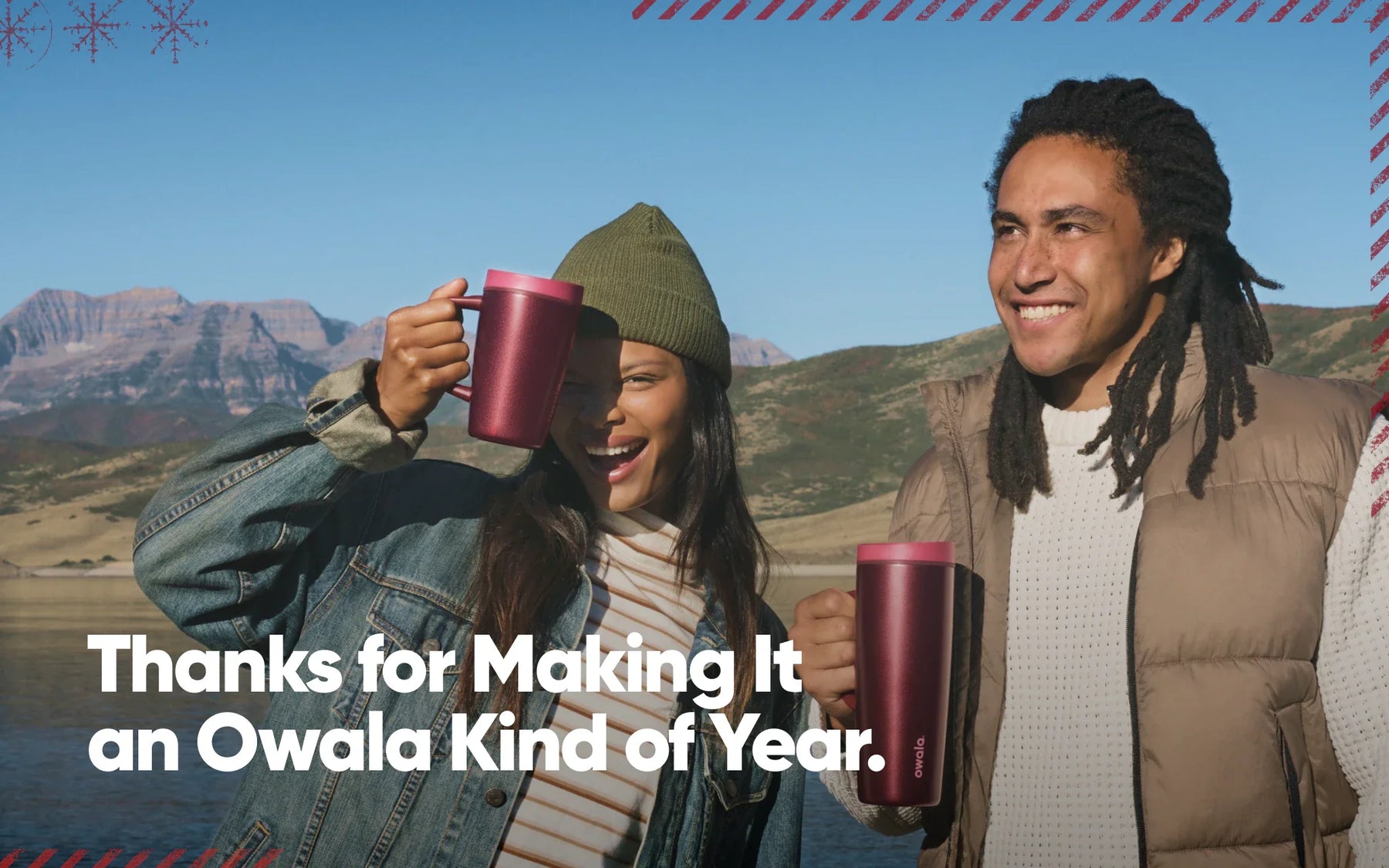 Smiling couple holding red Owala mugs and tumblers outdoors with mountain and lake scenery, with text overlay reading "Thanks for Making It an Owala Kind of Year"