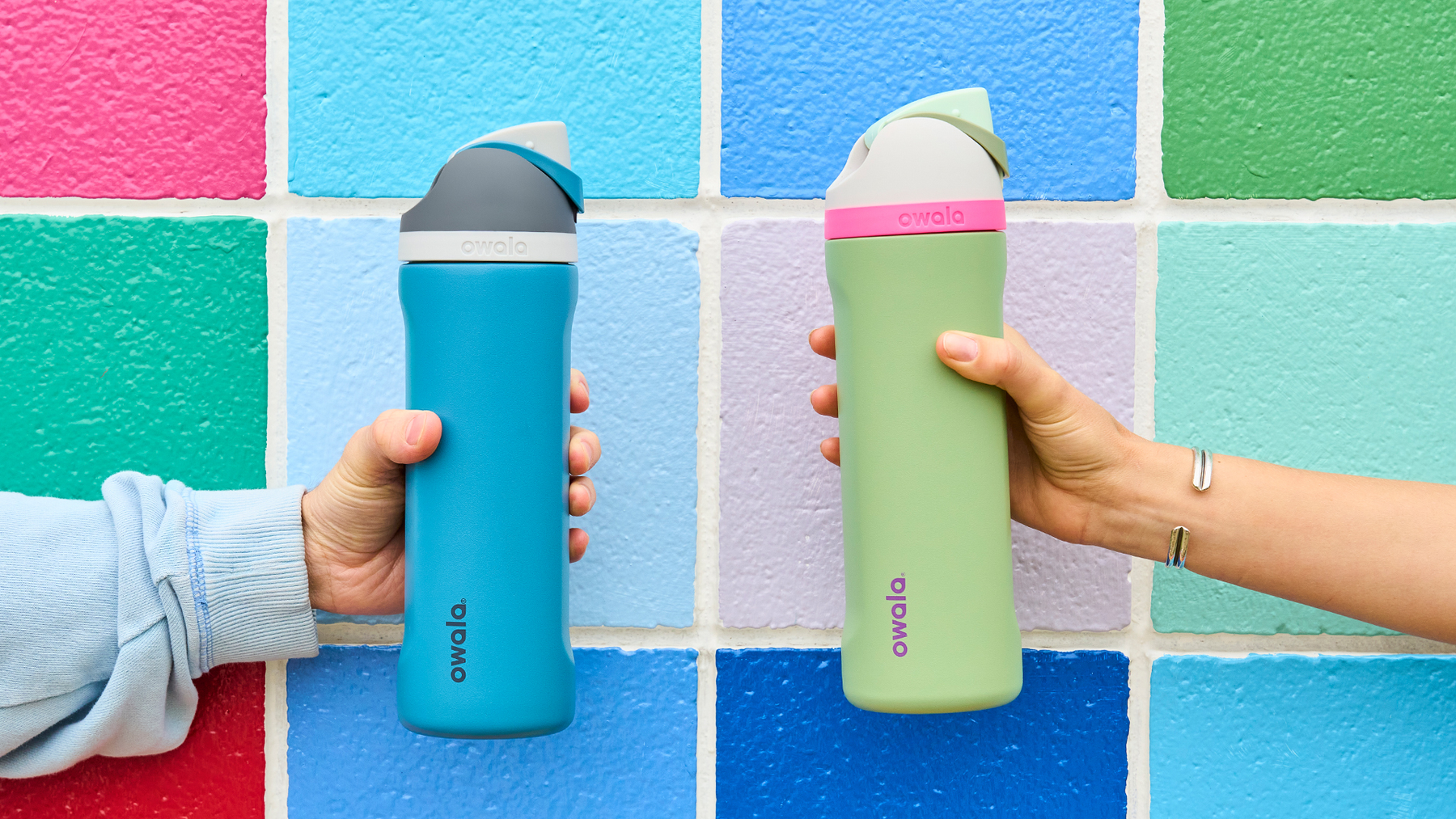 two people holding Owala bottles in front of a colorful wall